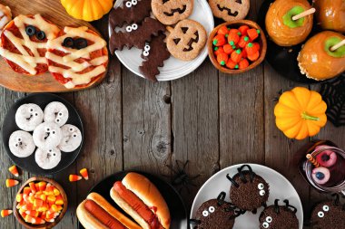 Cadılar Bayramı partisinin yemek çerçevesi koyu ahşap arka planda ve fotokopi alanı var. Manzaranın üstünde. Eğlenceli mumya pizzaları, parmak sosisliler, karamelli elmalar, kekler, şekerler, kurabiyeler ve çörekler..