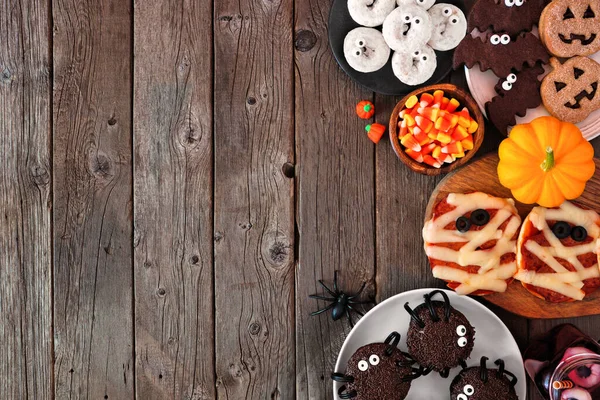 Halloween party food side border over a rustic wood background with copy space. Overhead view. Spooky mummy pizzas, cupcakes, candy, cookies and donuts.