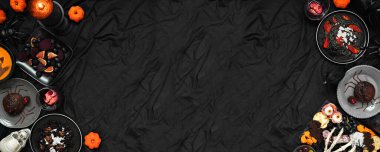 Cadılar Bayramı partisi, siyah pankartın arka planında çifte sınır oluşturdu. Üst Manzara. Ürkütücü şarküteri tahtası, siyah risotto ve makarna, örümcek pastası ve elma kafatası şarabı.