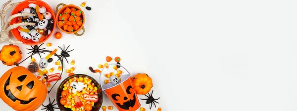 Halloween trick or treat corner border with jack o lantern pails and a selection of candy. Above view on a white banner background with copy space.