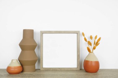 Düşen vazolarla ahşap çerçeve ve ahşap bir rafta ev dekorasyonu yap. Sonbahar konsepti. Beyaz bir duvara karşı kare çerçeve.