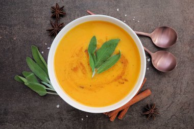 Fall pumpkin or squash soup with warms spice and herbs. Overhead view table scene on a dark background.