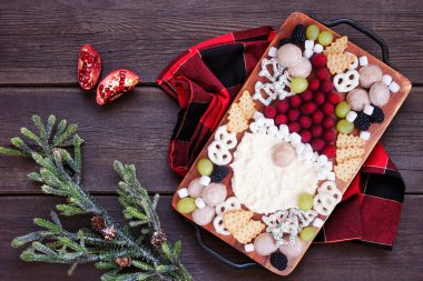 Noel Baba otlatma tahtası. Koyu bir ahşap arka planda, yukarıdaki masa manzarası. Tatil yemeği konsepti. Krem peynir, meyve, kraker ve tatlı..