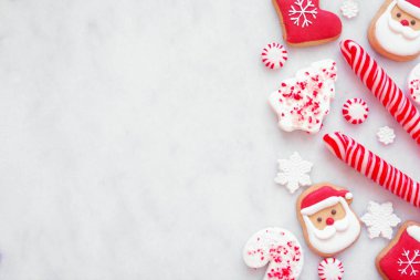 Noel tatlıları kırmızı ve beyaz kurabiyeler ve şekerlerle sınırda. Kopya alanı olan beyaz mermer bir arkaplan üzerinde genel görünüm.