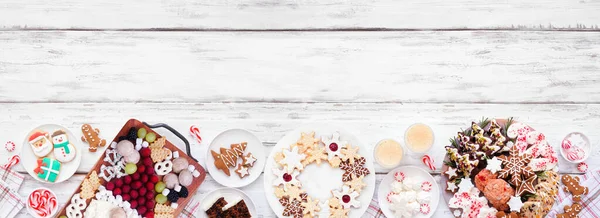 Noel kurabiyeleri ve tatlılar alt sınırda. Beyaz ahşap bir arka planda tepeden aşağı manzara. Noel Baba otlatma tahtası, kurabiye tabakları ve tatlı tabaklar. Boşluğu kopyala.