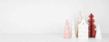 Pembe ve beyaz Noel evi ve beyaz bir rafta ağaç dekoru. Fotokopi alanı olan beyaz bir duvar afişi.