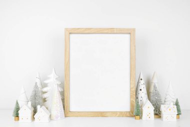 Noel, ahşap çerçeve, beyaz evler, yeşil ve beyaz Noel ağacı dekoru ile süslenir. Beyaz bir duvara dayalı beyaz bir raftaki portre çerçevesi. Boşluğu kopyala.