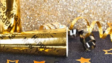 Parıldayan altın ve siyah bir arkaplanda yılbaşı partisi dekorasyonu. Yavaş yan çevirme hareketi. Ses çıkaranlar, kurdele, konfeti.