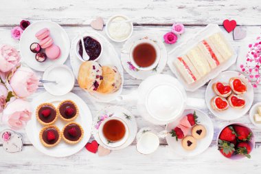 Sevgililer Günü ya da temalı öğleden sonra çayına bayılırım. Beyaz ahşap arka planda üst manzara sahnesi. Çeşitli parmak sandviçleri, tatlı tatlılar ve hamur işleri..