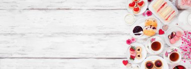 Sevgililer Günü ya da temalı öğleden sonra çayına bayılırım. Beyaz ahşap bir arka planda üst aşağı görüş kenarı sınırında. Çeşitli parmak sandviçler, tatlı tatlılar ve hamur işleri. Boşluğu kopyala.