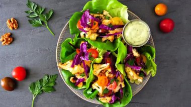 Kızarmış karnabahar, lahana ve domatesli sağlıklı marul ambalajı. Yavaş zum hareketi. Koyu bir arkaplan üzerinde üst görünüm.