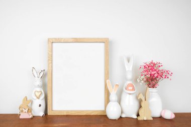 Paskalya evi dekorasyon sahnesi. Tahta bir rafta paskalya tavşanları, yumurtalar ve pembe çiçeklerle portre çerçevesi yap. Boşluğu kopyala.