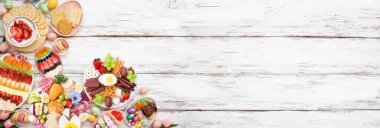 Bahar ya da Paskalya otlatma kurulu temalı bir köşe kenarı beyaz ahşap bir afişe karşı. Genel bakış. Tatlı ve peynir, et ve meyve aperatifleri. Boşluğu kopyala.