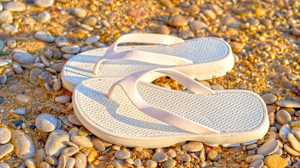 White beach shoes on a background of sand and pebbles.