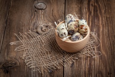 Ahşap masa üzerinde ahşap bir kapta çiğ bıldırcın yumurtası.