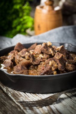 Dökme demir tavada sığır güveci, ahşap arka plan. Sığ alan derinliği.