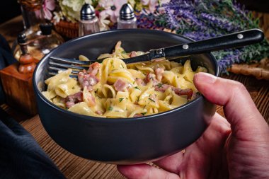 Tagliatelle Carbonara 'yı ahşap masada kasede yosunluyor. Sığ alan derinliği.