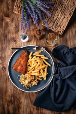 Kızarmış balık fileto, patates kızartması ve mavi tabakta salata. Üst görünüm.