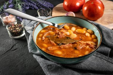 Domates soslu fasulye, pastırma ve siyah kasede sosis. Seçici odak.