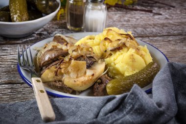 Kızarmış ciğer, soğan ve elma haşlanmış patates ve salatalık turşusuyla servis edilir..