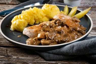 Mantar soslu ızgara tavuk göğsü, patates püresi ve salatalık turşusu ile servis edilir..