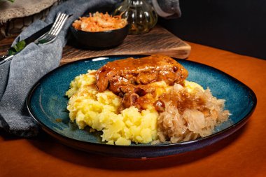 Patates püresi ve lahana turşusuyla servis edilen baharatlı soslu domuz pirzolası. Sığ alan derinliği.