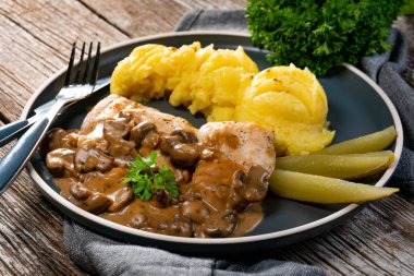 Mantar soslu ızgara tavuk göğsü, patates püresi ve salatalık turşusu ile servis edilir..