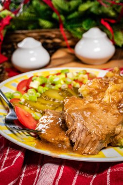 Kendi sosunda haşlanmış domuz eti patates püresi, domates ve salatalık turşusuyla servis edilir..