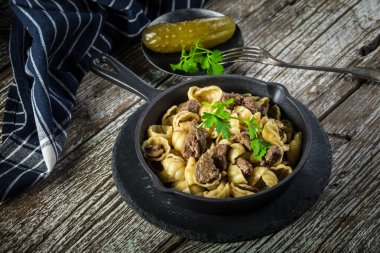 İtalyan makarna kabukları ve biftek sosu ahşap masada dökme demir tavada..