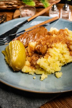 Kendi sosunda haşlanmış domuz eti patates püresi ve salatalık turşusuyla servis edilir..