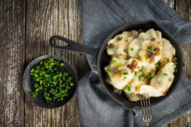 Fırında hamur köftesi (pierogi), içinde dökme demir tavada yeşillikler serpiştirilmiş..