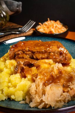Patates püresi ve lahana turşusuyla servis edilen baharatlı soslu domuz pirzolası. Sığ alan derinliği.