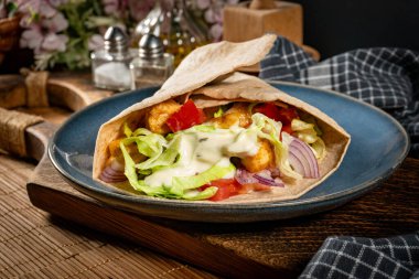 Kızarmış tavuk ve sebzeli salata. Baharatlı yaban turpu sosu ile sarılmış tortilla..