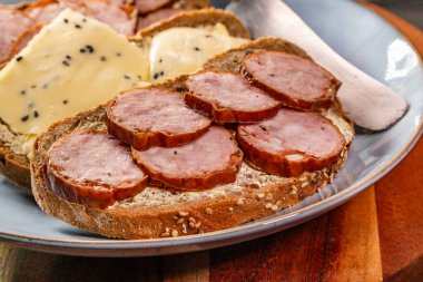 Peynirli ekmek dilimleri ve mavi tabakta sosis..