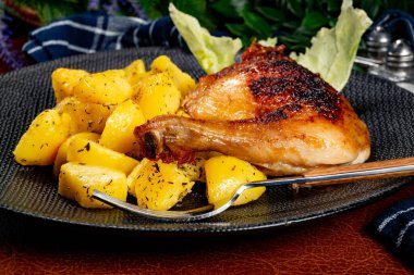 Appetizing baked chicken leg quarter with browned skin served with crispy fries for dinner.