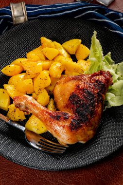 Appetizing baked chicken leg quarter with browned skin served with crispy fries for dinner.