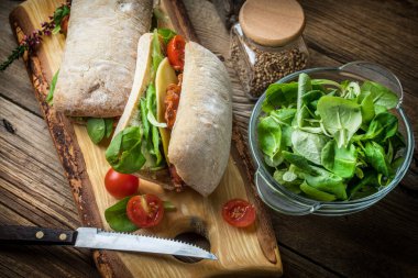 Ahşap tahta üzerinde Roka Salatası, pastırma ve sarı peynirli ciabatta sandviç.