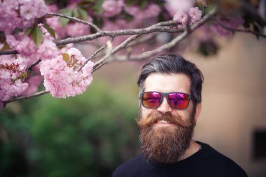 Karizmatik sakallı, uzun bıyıklı, gri saçlı, koyu renk kazaklı ve bahar aylarında kiraz çiçeklerinin yanındaki parlak gözlüklü adam..