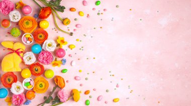 Paskalya yumurtaları, tavşancık, şeker ve pastel pembe arka planda renkli bahar çiçekleri. Metin için fotokopi alanı olan en az tatil konsepti. Düz uzanma deseni.