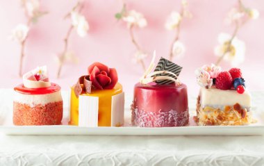 Beyaz tabakta çeşitli mini kekler. Tatil için taze böğürtlen ve çiçeklerle süslenmiş şekerler..