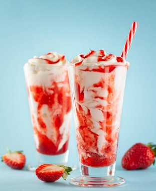 Çilekli milkshake, çırpılmış krema ve böğürtlen şurubu mavi arka planda uzun bardakta..
