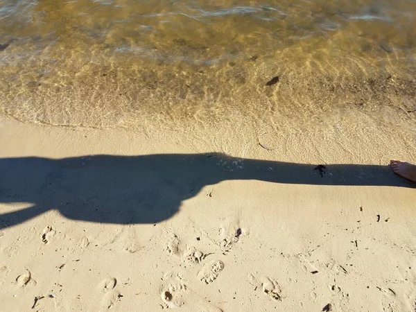 해변 모래 위에서 물과 함께 있는 사람의 그림자 — 스톡 사진