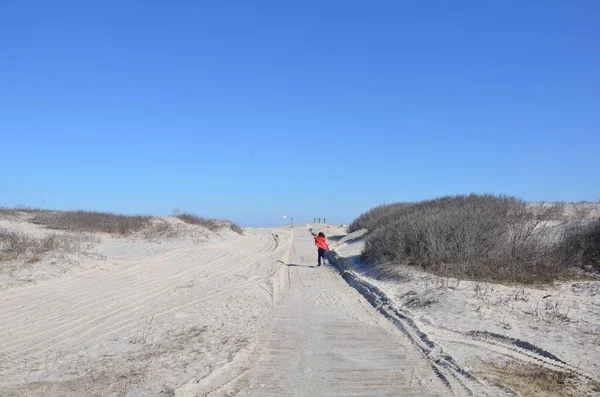 Niño en abrigo rojo corriendo en camino de arena en la playa — Foto de Stock