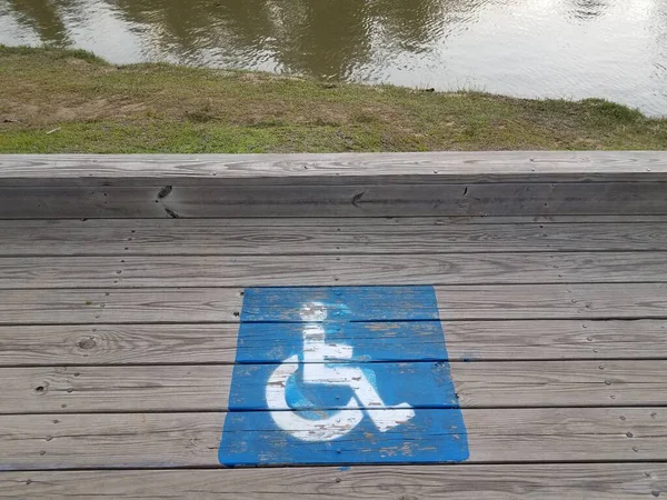 Logotipos de silla de ruedas azul en el paseo marítimo de madera cerca del río —  Fotos de Stock