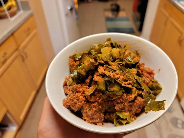 Hand holding bowl of Ethiopian food raw beef and greens — Stock Photo, Image