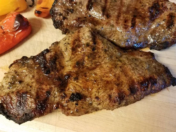 Carne de frango grelhada em tábua de corte de madeira com pimentas — Fotografia de Stock