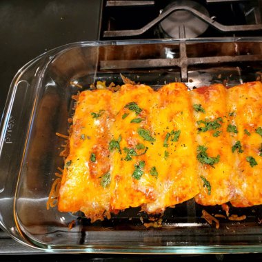 Sobanın üzerindeki cam kabın içinde peynirli sıcak enchilada.