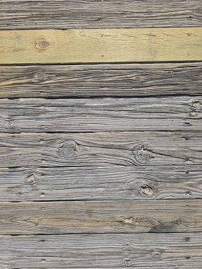 Çeşitli tahıl desenleri, düğümler ve doğal kusurları olan eski ahşap tahtalar. Yüzeyde gri ve kahverengi tonların bir karışımı var, daha açık, sarımsı bir kalas öne çıkıyor, bu da yeni bir eklenti olduğunu gösteriyor.