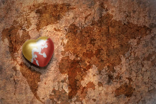 Heart with national flag of bhutan on a vintage world map crack paper background. — Stock Photo, Image