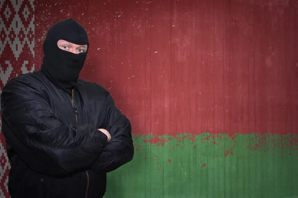 Om periculos într-o mască în picioare lângă un zid cu steagul național pictat de belarus — Fotografie, imagine de stoc